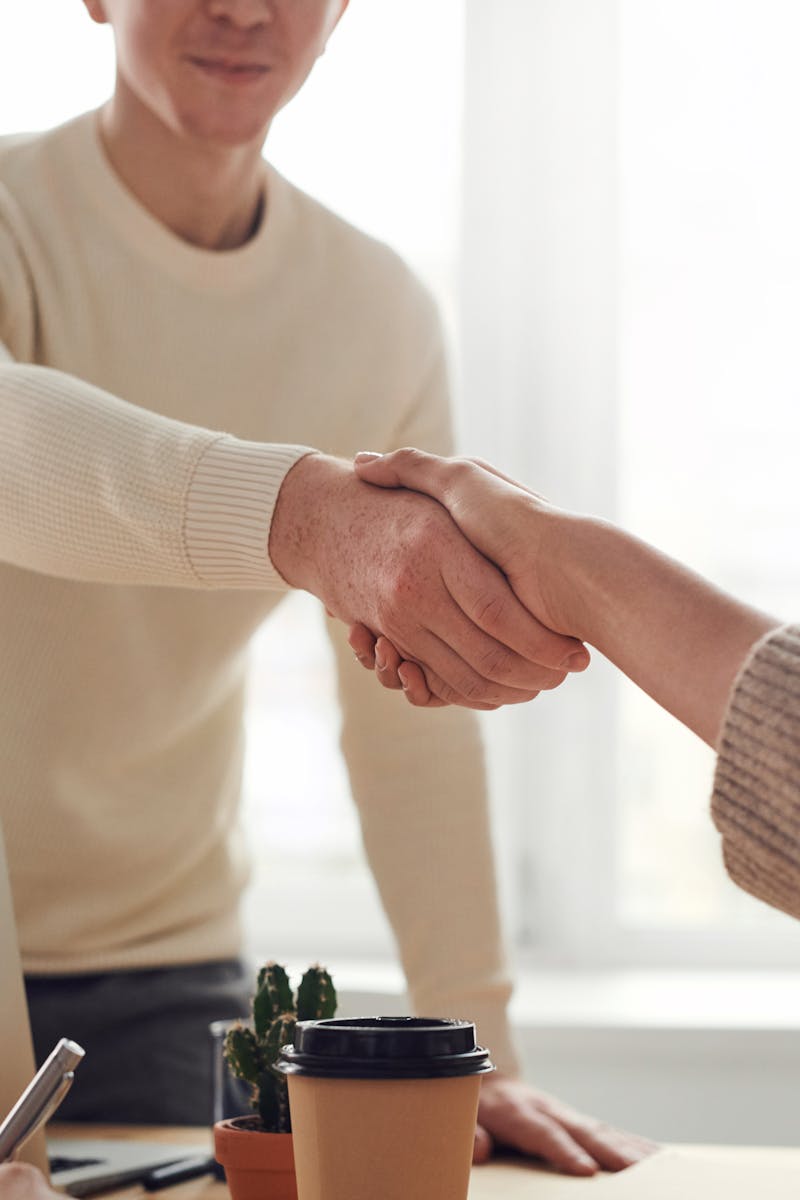 pexels-photo-3184465-3184465 Close-up of professionals shaking hands over coffee in a modern office.